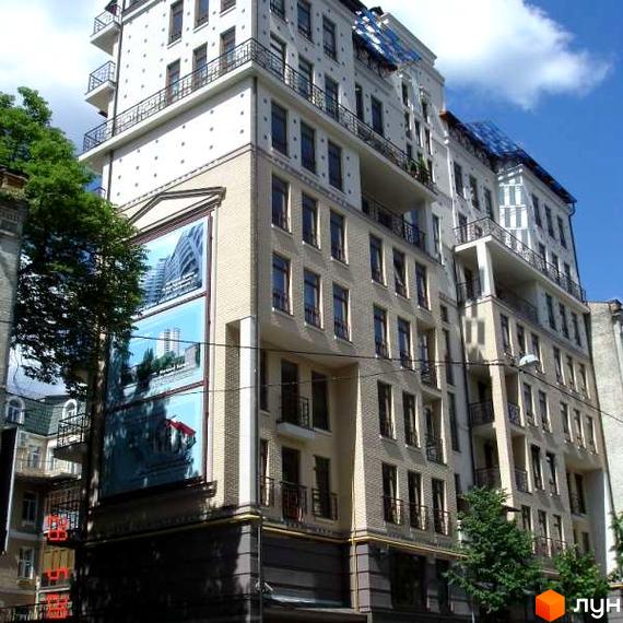 Зовнішній вигляд житлового комплексу Гончара 22 з фасадом зі світлої цегли та великими вікнами. На фасаді розміщені рекламні банери з зображеннями будівель.