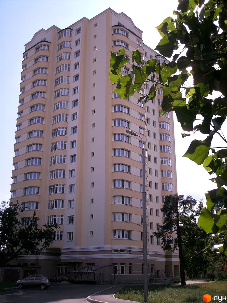 Новобудова на вул. Гашека, 8а: багатоповерховий будинок світлого кольору з вигнутими балконами. Прибудинкова територія з деревами та дорогою.