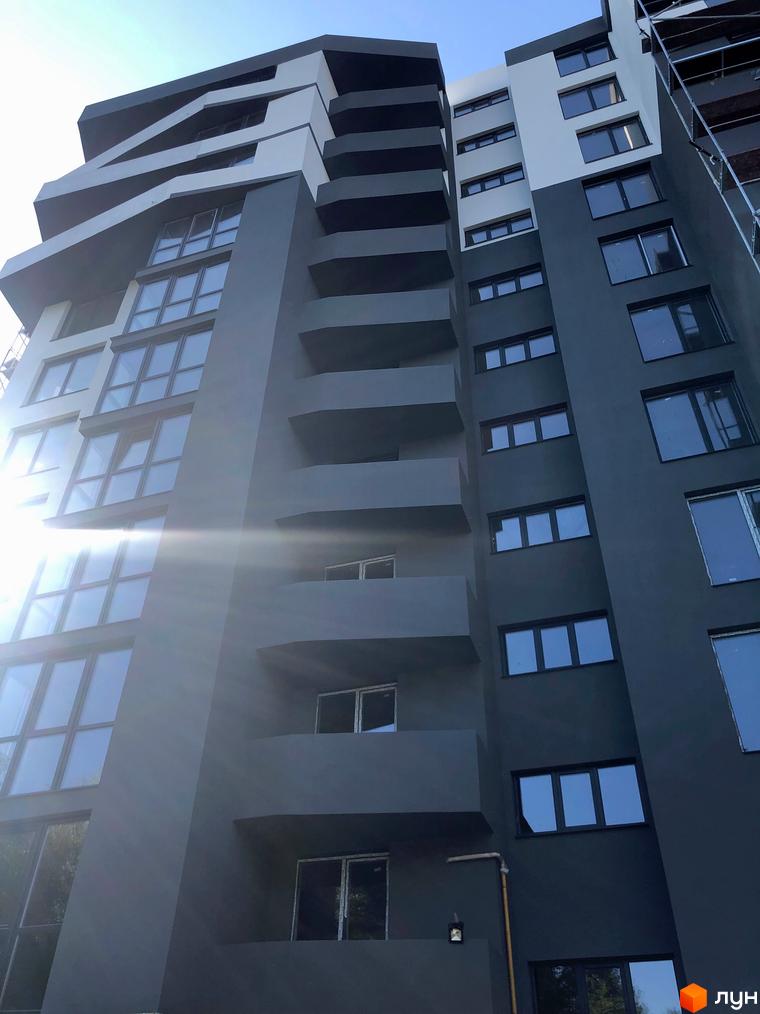 Зовнішній вигляд новобудови ЖК Грін Парк з сірими та білими фасадами та великою кількістю вікон. Будинок має незвичайну архітектуру з виступаючими балконами.