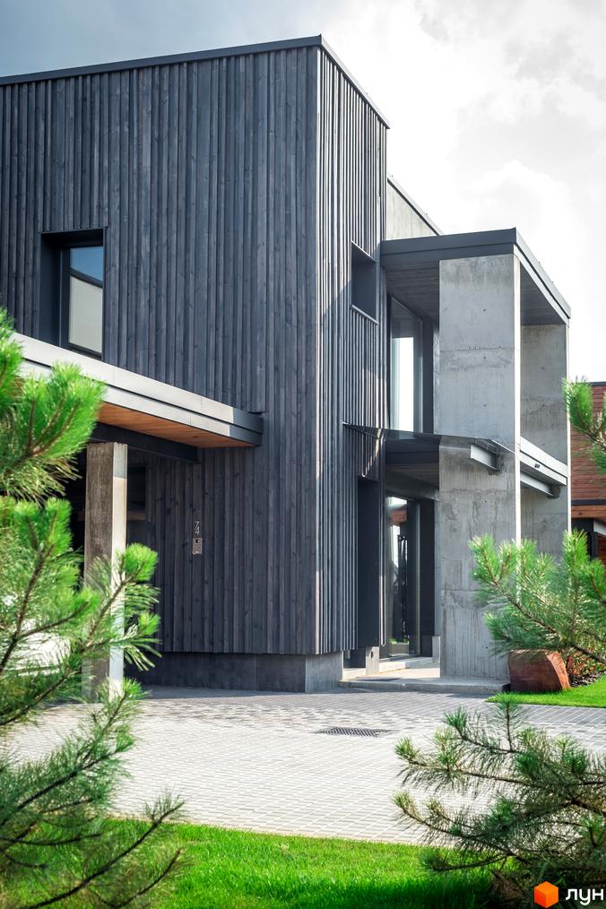 Котеджне містечко На Щасливій: фасад будинку з темного дерева та бетону, вимощена територія та зелена галявина.