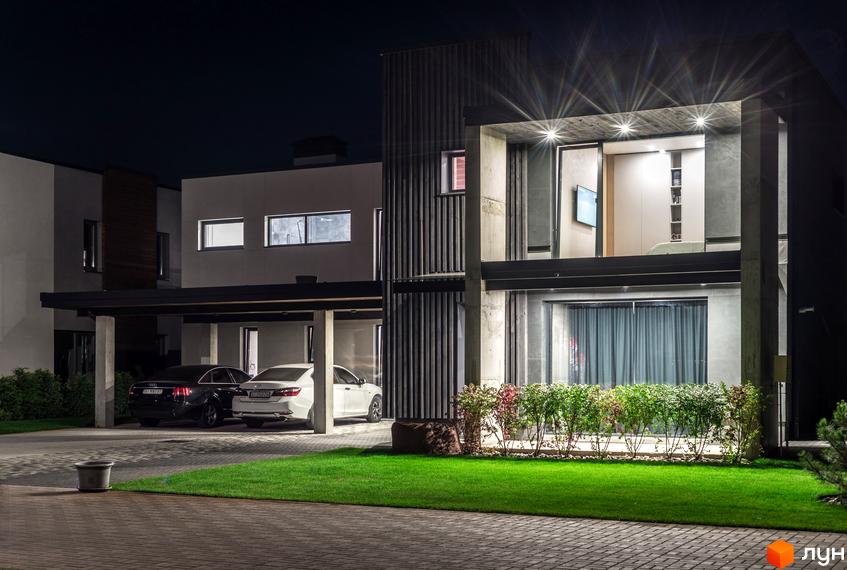 Котеджне містечко На Щасливій: двоповерховий будинок з панорамними вікнами та навісом для двох автомобілів. Прибудинкова територія з газоном та кущами.