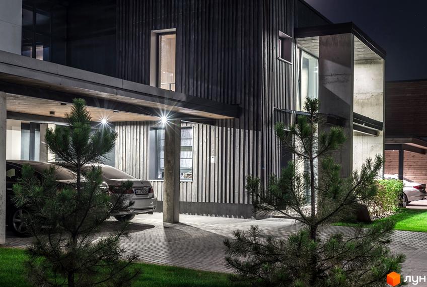 Котеджне містечко На Щасливій: екстер'єр будинку з дерев'яною обшивкою та бетонними елементами вночі. Прибудинкова територія з паркуванням та зеленими насадженнями.