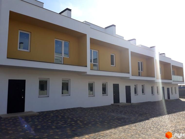 Зовнішній вигляд житлового комплексу Domino Townhouse з білими фасадами та жовтими вставками, з прибудинковою територією, вимощеною бруківкою.