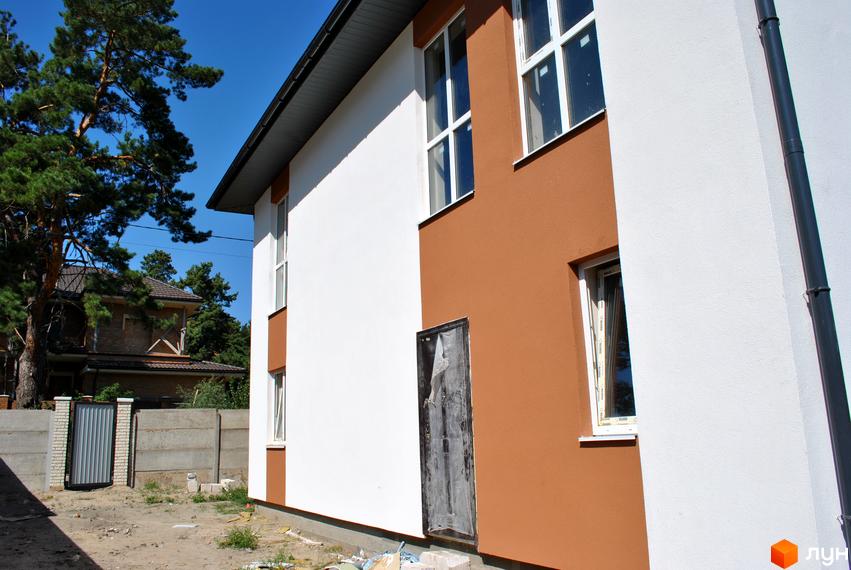 Фасад новобудови на вул. Івана Франка, 34-36, з білою та коричневою штукатуркою, вікнами та прибудинковою територією з парканом та деревами.