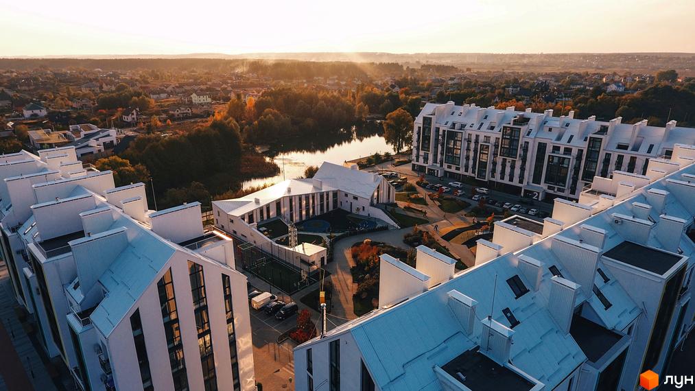Житловий комплекс City Lake: білі багатоповерхові будинки з оригінальними дахами та великими вікнами, розташовані біля озера з облаштованою територією.