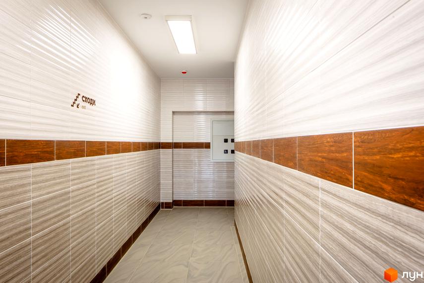 Коридор житлового комплексу Lystopad з білою плиткою та коричневими вставками. На стіні знак 