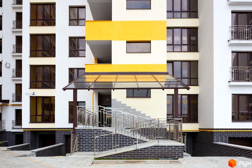 Житловий комплекс Lystopad: будівля з білими та жовтими фасадами, вікнами та балконами. Вхід має скляний навіс, пандус та сходи.
