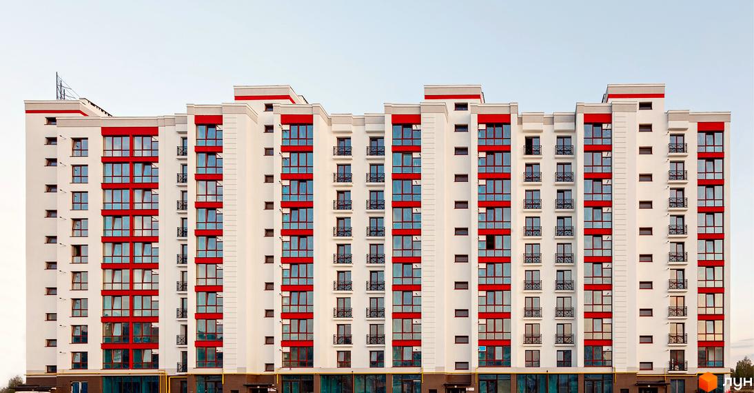 Висотна новобудова з білими фасадами та яскравими червоними акцентами. На фасаді багато вікон, деякі з балконами.