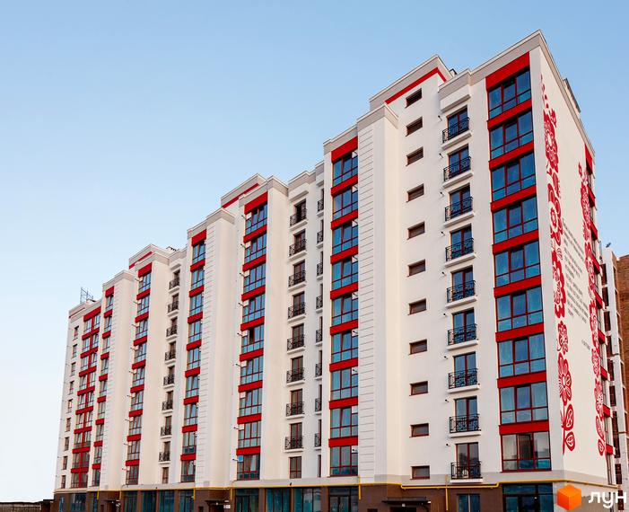 Житловий комплекс Містечко Козацьке: багатоповерховий будинок з білим фасадом, червоними віконними рамами та балконами. На торці будівлі великий червоний орнамент.