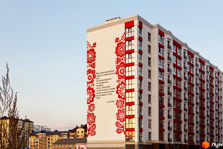 Висотна будівля Житлового комплексу Містечко Козацьке з червоними акцентами на фасаді. На стіні зображено вірш з квітковим орнаментом.