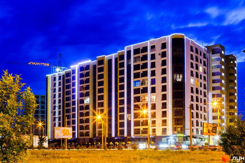Житловий комплекс Lystopad з підсвіченими фасадами вночі. Навколо будинку зелена територія та освітлення.