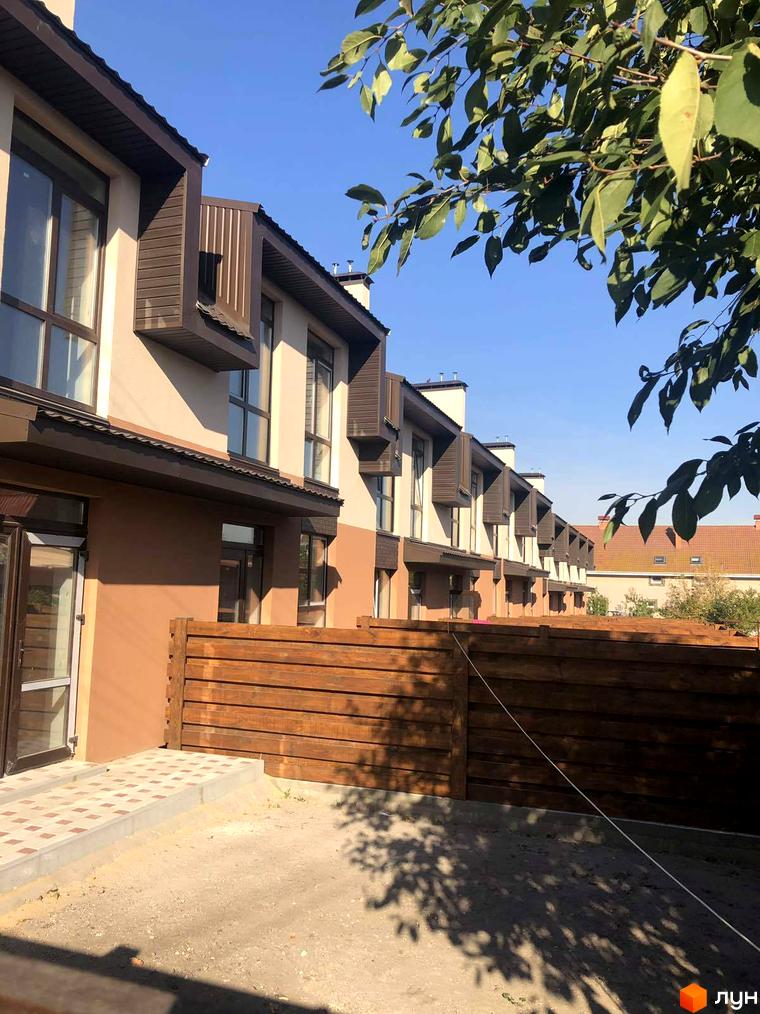 Зовнішній вигляд таунхаусів в Житловому комплексі „Озерний“ з коричневими дахами та дерев'яним парканом на прибудинковій території.