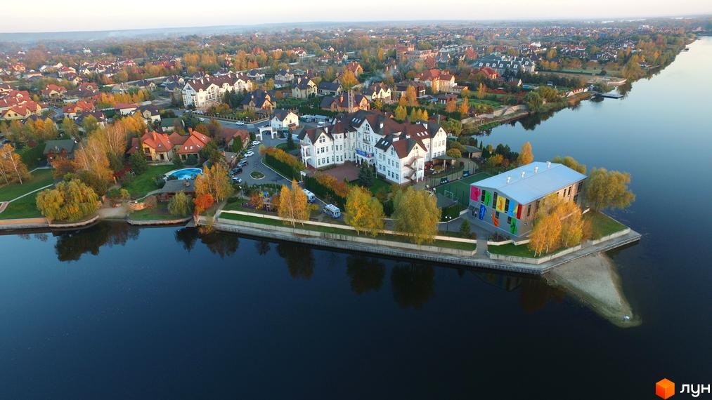 Вид на котеджне містечко КМ Золоче з висоти пташиного польоту. Білі будинки з червоними дахами розташовані біля води, навколо зелені дерева.