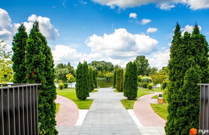 Вид на доглянуту територію Містечко котеджів Золоче з алеями, газонами та деревами. Яскраве небо з хмарами.