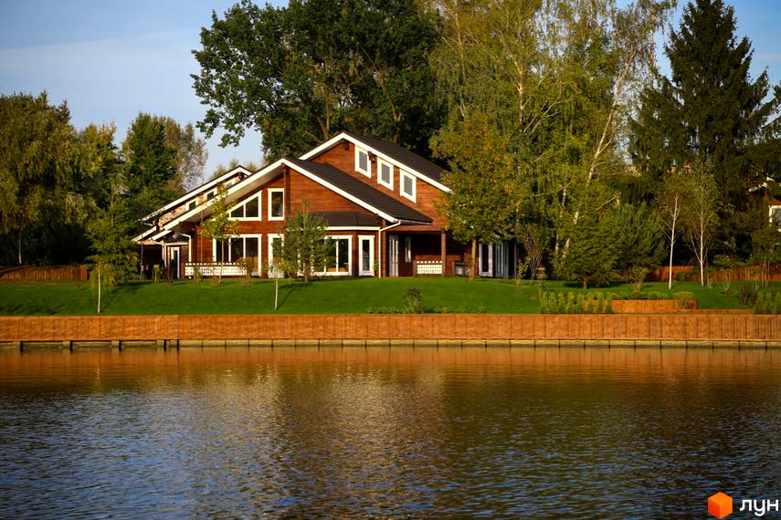 Дерев'яний будинок у Котеджному містечку Riverside Family Club з великою кількістю вікон, розташований біля води на доглянутій ділянці.