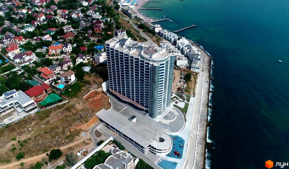 Вид на висотний житловий комплекс Морська симфонія з панорамними вікнами на узбережжі. Поруч розташовані будинки меншої поверховості та облаштована набережна.