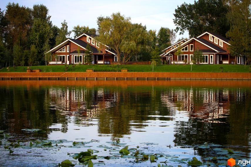 Котеджне містечко Riverside Family Club: двоповерхові будинки з дерев'яним фасадом на березі річки. Прибудинкова територія з газоном та дерев'яною набережною.