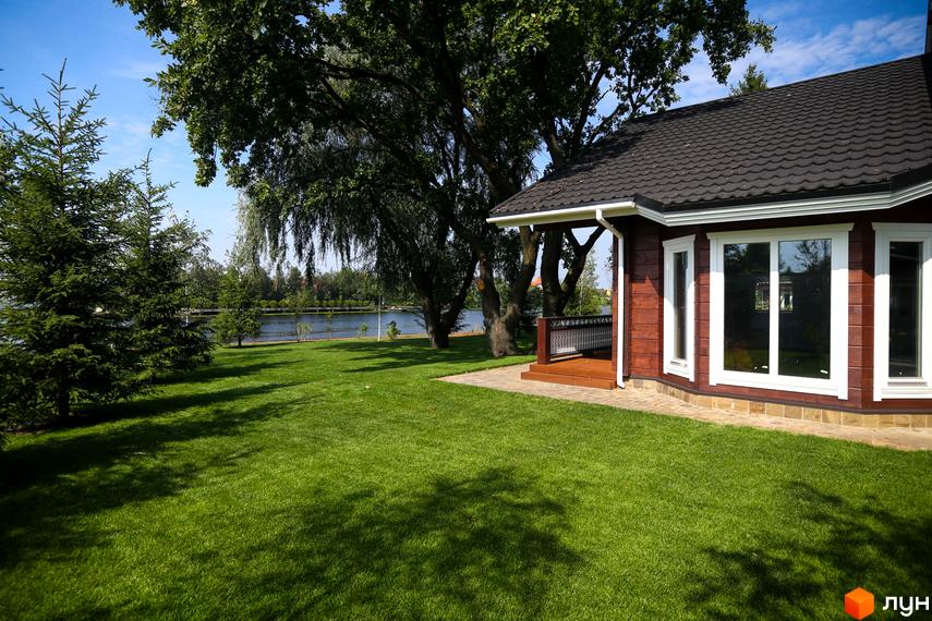 Котеджне містечко Riverside Family Club з дерев'яним фасадом та великими вікнами, розташований на доглянутій зеленій галявині біля озера.