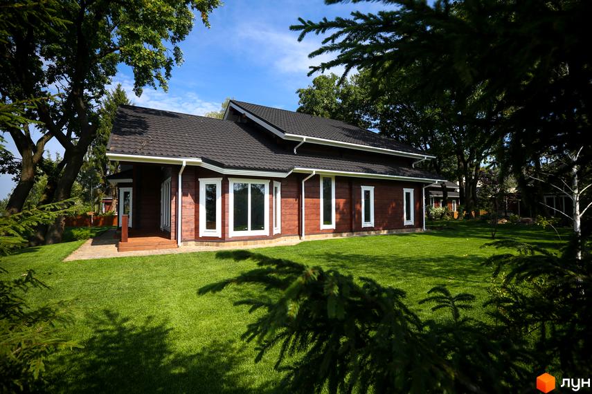 Котеджне містечко Riverside Family Club. Двоповерховий дерев'яний будинок з великими вікнами та темним дахом, оточений зеленою галявиною та деревами.