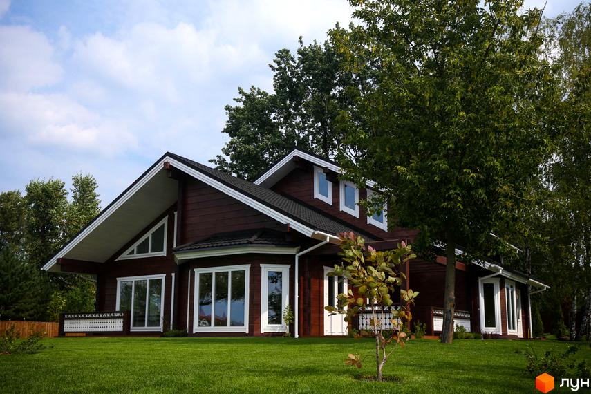 Котеджне містечко Riverside Family Club: коричневий дерев'яний будинок з білими вікнами та дахом, оточений зеленню та доглянутим газоном. Зовнішній вигляд будинку та прибудинкова територія.