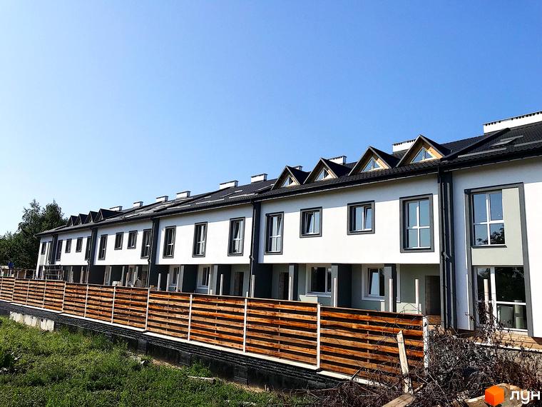 Фасад новобудови на вул. Володимирська (Червоного орача), 3, з дерев'яним парканом та зеленою зоною.