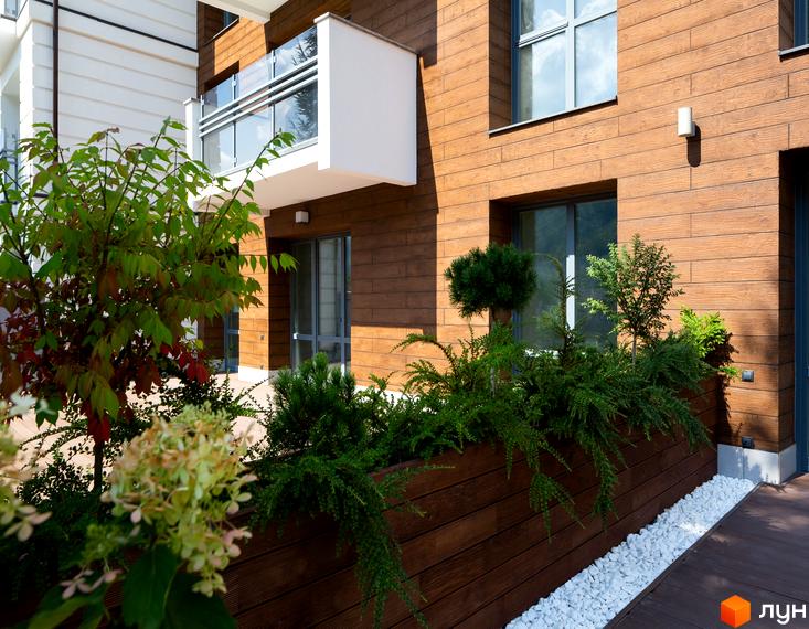 Новобудова Крайобраз з дерев'яним фасадом та зеленою зоною відпочинку. Балкон з скляною огорожею та квітами на прибудинковій території.