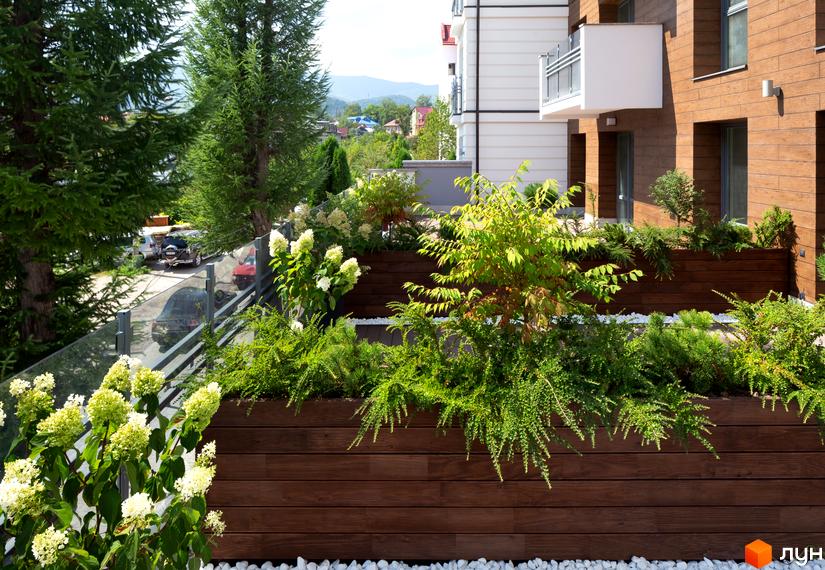 Житловий комплекс Крайобраз з озелененою терасою та видом на гори. Сучасна архітектура новобудови з дерев'яними елементами фасаду та скляними перилами.