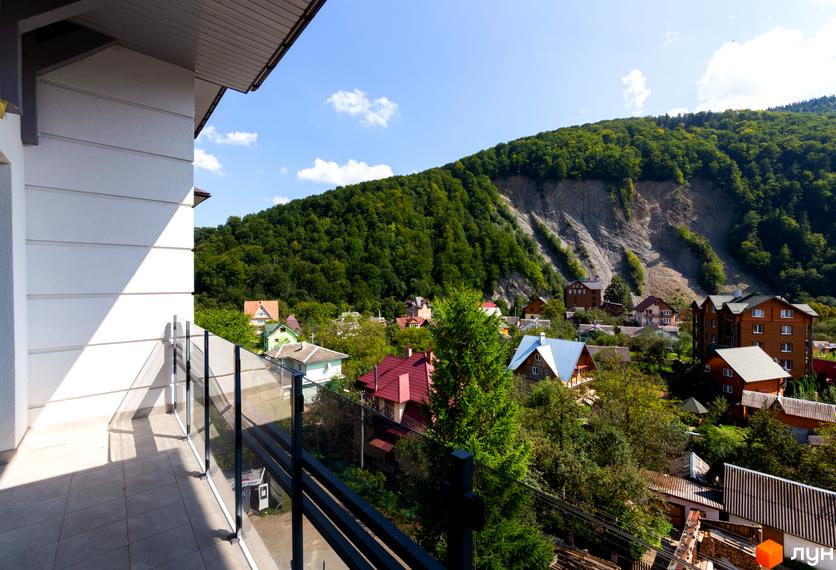 Вид з балкона на житловий комплекс Крайобраз, що розташований серед зелених гір. Будинки з червоними та сірими дахами оточені деревами.