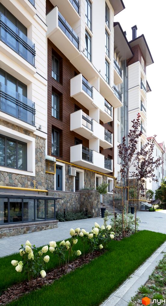 Новобудова ЖК Крайобраз: фасади з дерев'яними вставками та скляними балконами. Доглянута прибудинкова територія з клумбами та газоном.