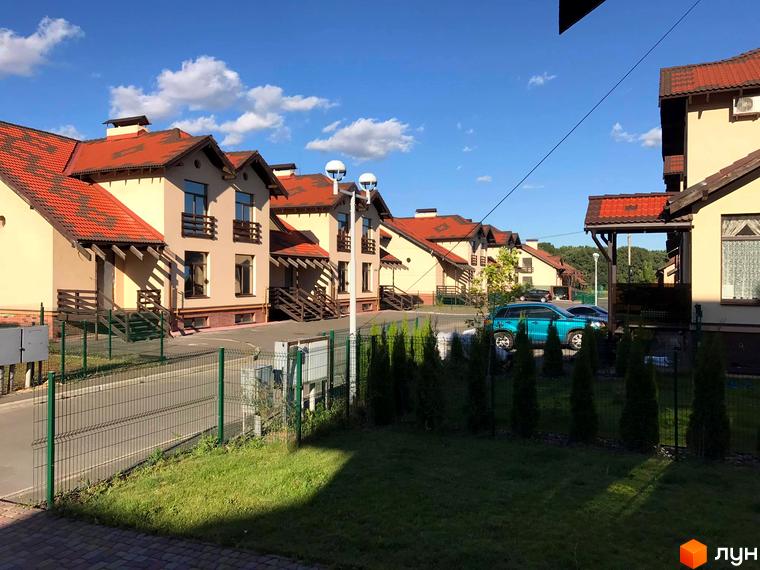 Зображення сторінки Котеджного містечка Садок Вишневий. На фото будинки з червоними дахами та доглянута прибудинкова територія з газоном та деревами.