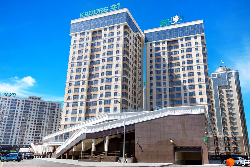 Високі будинки житлового комплексу KADORR 41 з великою кількістю вікон. На території комплексу є підземний паркінг та пішохідні зони.