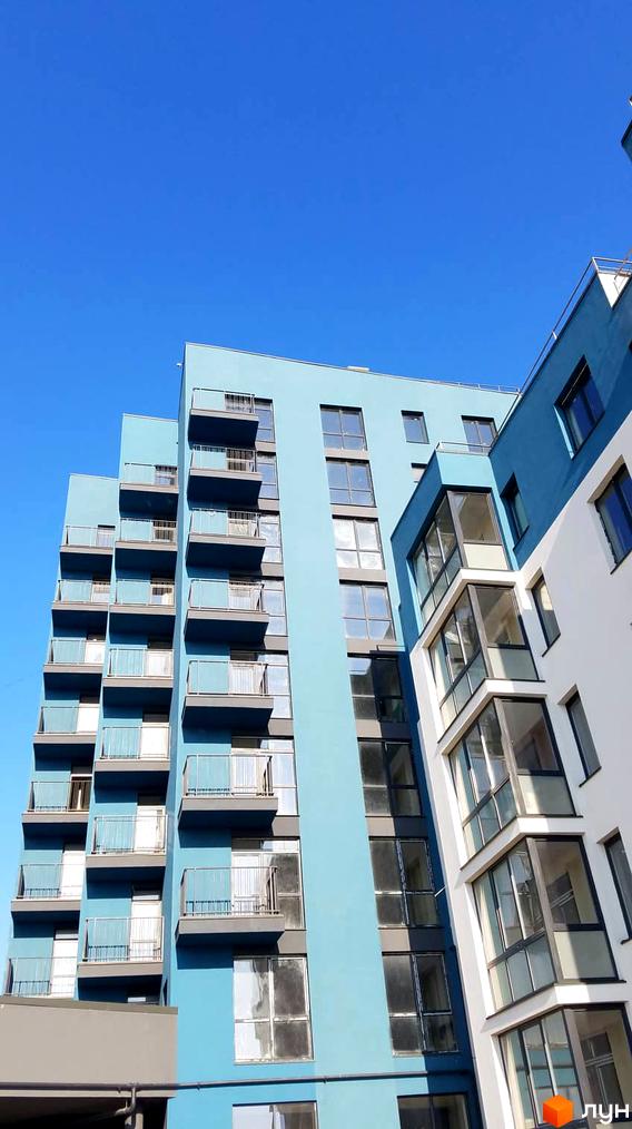 Житловий комплекс Басів схил: багатоповерховий будинок блакитного кольору з балконами та великими вікнами під чистим небом.