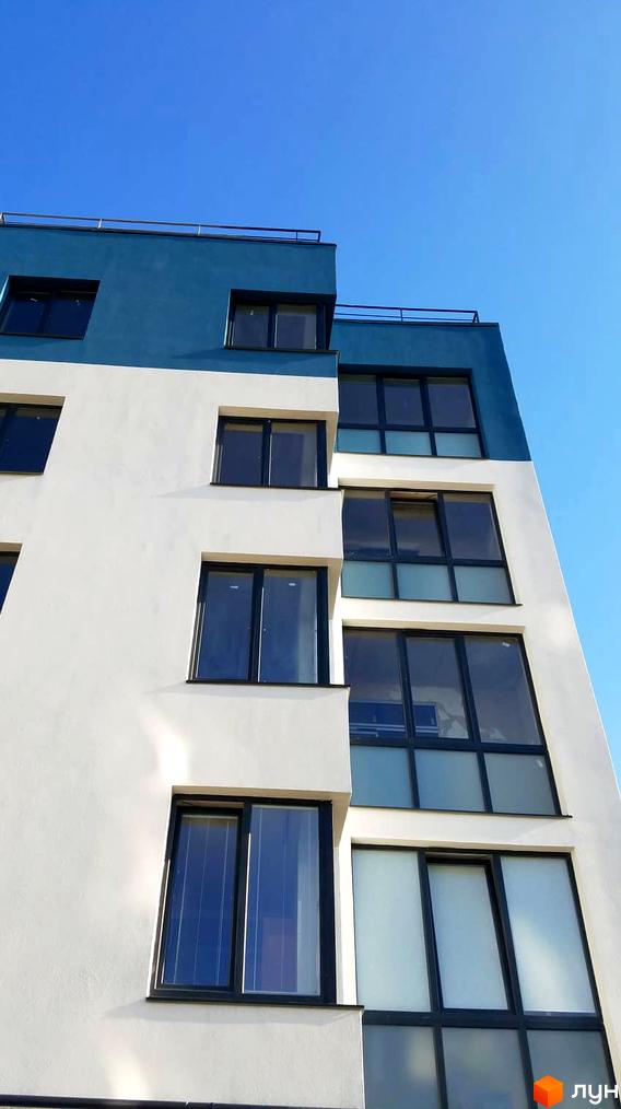 Житловий комплекс Басів схил: багатоповерховий будинок з білим та синім фасадом та темними віконними рамами на тлі блакитного неба.