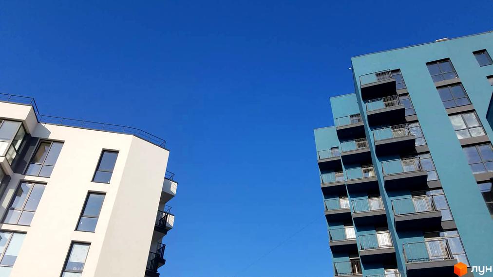 Новобудова Басів схил: дві багатоповерхові будівлі, біла та блакитна, з балконами та вікнами на тлі синього неба.