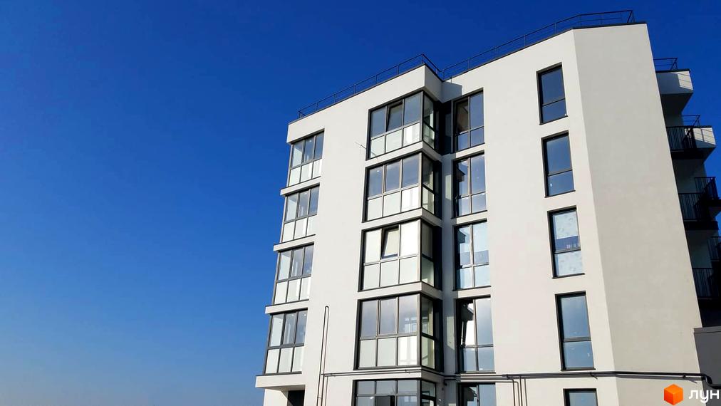 Новобудова ЖК Басів схил з панорамними вікнами та балконами на фоні блакитного неба. Зовнішній вигляд будинку з білою фасадною штукатуркою та темними рамами вікон.