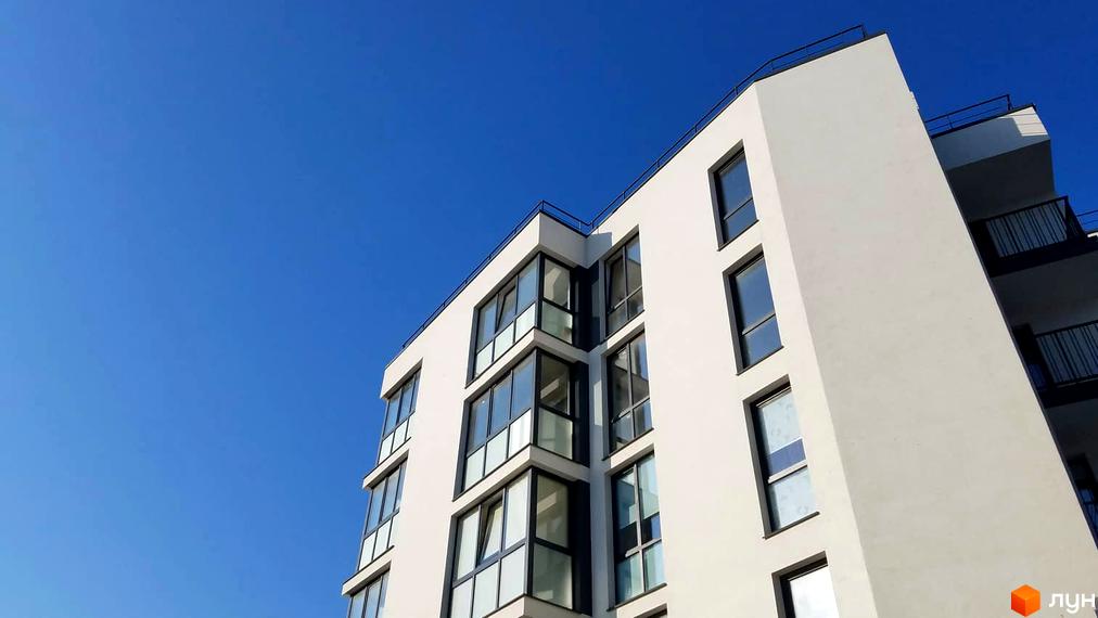 Новобудова ЖК Басів схил з панорамними вікнами та балконами на фоні блакитного неба. Зовнішній вигляд сучасної будівлі.