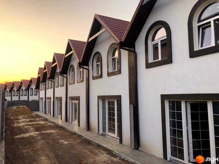 Ряд таунхаусів з білими стінами та коричневими дахами. На передньому плані - земляна ділянка.