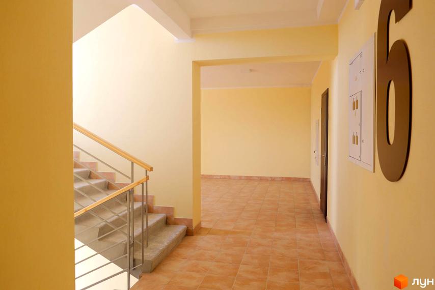 Сходова клітка та коридор у новобудові Житлового комплексу Апельсин. Приміщення має світлі стіни, плиткову підлогу та металеві перила.