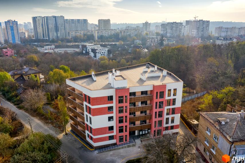 Житловий комплекс Козацький Гай: багатоповерхова новобудова з червоно-білим фасадом та балконами. Навколо – прибудинкова територія з деревами.