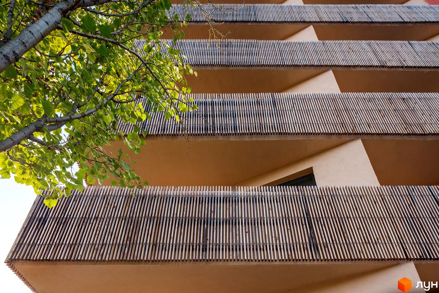 Фасад житлового комплексу Козацький Гай з дерев'яними елементами на балконах. Зелене дерево з листям біля будівлі.