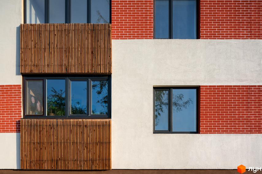 Фасад житлового комплексу Козацький Гай з червоної цегли та дерев'яними елементами. Вікна з відображенням дерев.