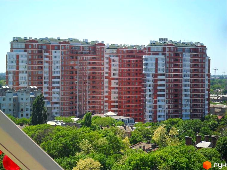 Житловий комплекс Капітан з червоною фасадною обробкою та зеленими насадженнями на прибудинковій території.