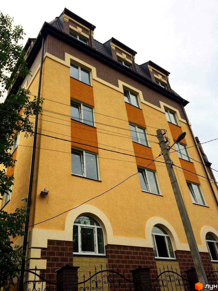 Фасад житлового комплексу Еко Таун з жовтими та коричневими елементами, вікнами та дахом. Навколо будівлі видно дерева та паркан.