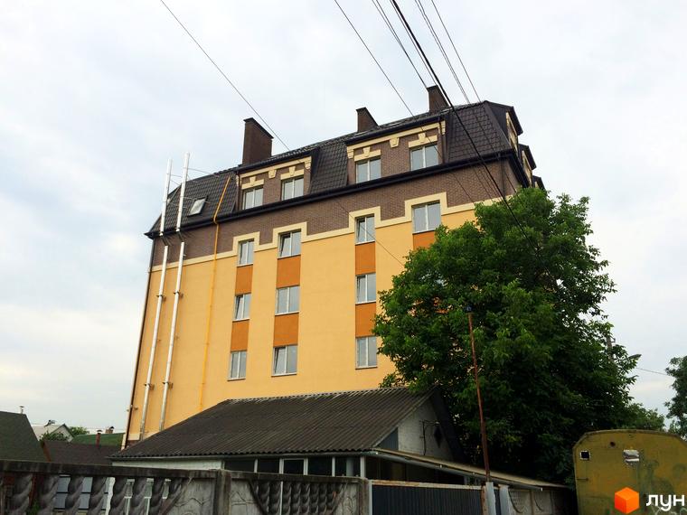 Житловий комплекс Еко Таун: багатоповерховий будинок з жовтою та цегляною обробкою, вікнами та темним дахом. Поруч зелене дерево та паркан.