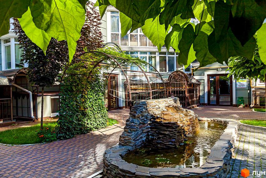 Житловий комплекс Британіка: зелена прибудинкова територія з фонтаном та арками. Зовнішній вигляд будинку з вікнами та дверима.