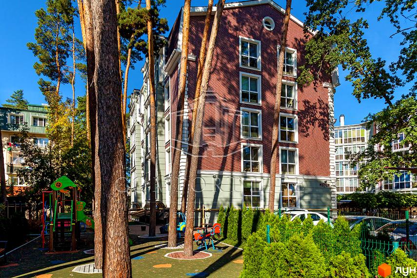 Новобудова ЖК Британіка з червоної цегли з великими вікнами. На прибудинковій території дитячий майданчик та зелені насадження.