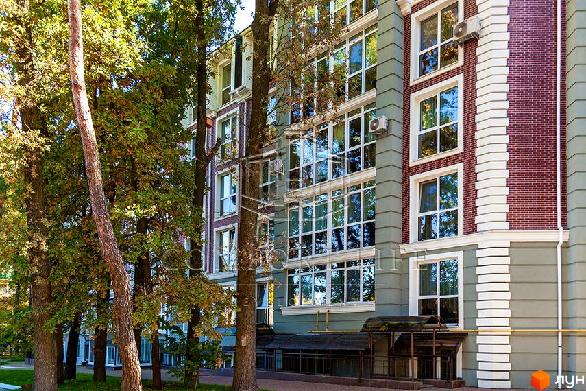 Новобудова Британіка з цегляним фасадом та великими вікнами, оточена деревами. Зовнішній вигляд будівлі з елементами декору та кондиціонерами.