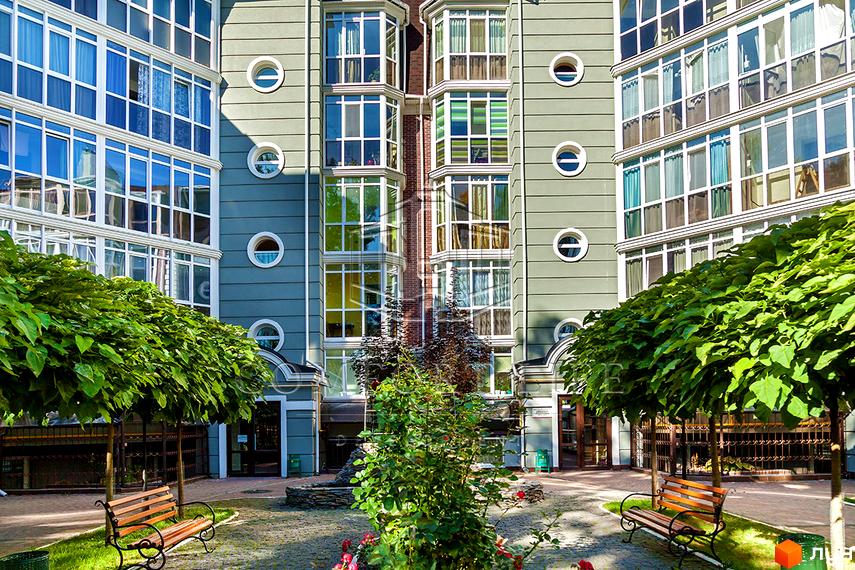 Житловий комплекс Британіка: зелена будівля з панорамними вікнами та круглими декоративними елементами. Прибудинкова територія з лавками та деревами.