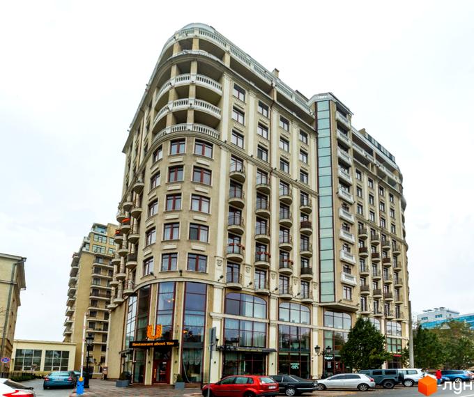 Житловий комплекс Будинок №1 - це багатоповерхова будівля з балконами та великими вікнами. На першому поверсі розташований ресторан. Навколо будівлі є прибудинкова територія з деревами та припаркованими автомобілями.