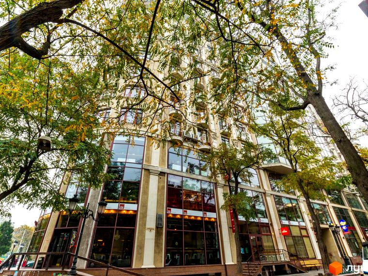 Житловий комплекс Будинок №1. Фасад будівлі з великими вікнами та елементами декору, оточений деревами з осіннім листям.